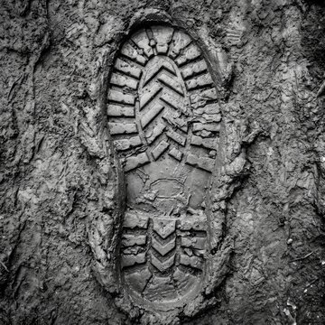 Close up of a muddy boot print in wet soil showing a detailed tread pattern in black and white