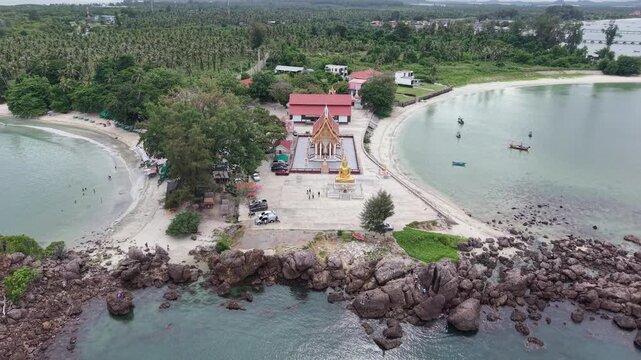 High angle aerial drone video featuring smooth dolly out movement revealing a coastal temple and sandy beach with rocky shorelines in Bang Saphan, Prachuap Khiri Khan, Thailand
