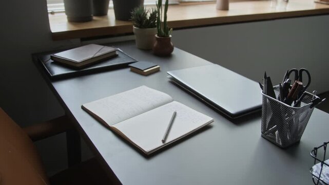 Organized office desk with open notebook, pencil, closed laptop, and stationery supplies. Footage suitable for corporate productivity concepts and remote work campaigns