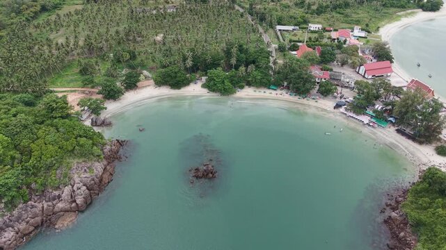 Aerial dolly out and tilt up revealing a picturesque twin headland cove vibrant beachside temple and vast coastal panorama in Bang Saphan, Prachuap Khiri Khan, Thailand