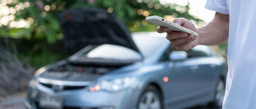 breakdown, broken car, repair. Man uses mobile phone check insurance premiums through application due to car accident . Find garage to get car fixed during country tour, waiting for help, emergency.