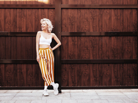 Young beautiful smiling hipster woman in trendy summer clothes. Sexy carefree model posing on the street background at sunset. Positive blond female. Cheerful and happy. Full length