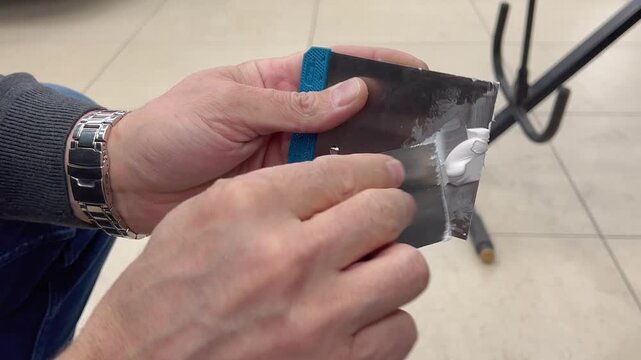 Professional auto mechanic man hands mixing two component polyester car body filler putty with a steel spatula knife tool. Professional vehicle bodywork repair, scratch, dent restoration. 