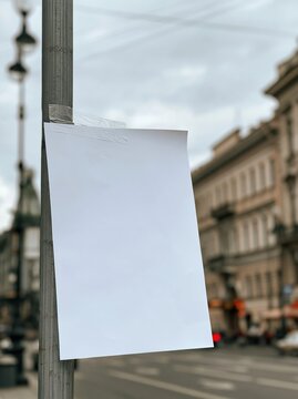Blank White Paper Attached to Street Lamp Pole in Urban Cityscape with Buildings and Cloudy Sky