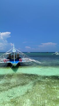 Vertical drone ascends and pans left during a flyover, revealing Doljo Beach, turquoise reef waters, boats, and the Panglao coastline in Bohol