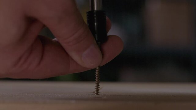 Close-up of a power screwdriver driving a metal wood screw into a wooden board during construction or furniture assembly.