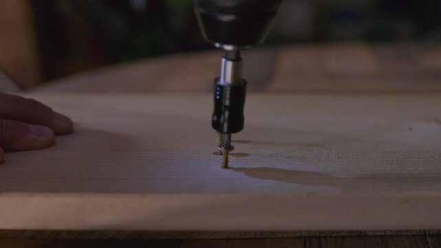 Close-up of a power drill fastening a screw into a wooden board, illustrating woodworking, construction, DIY and home improvement work.
