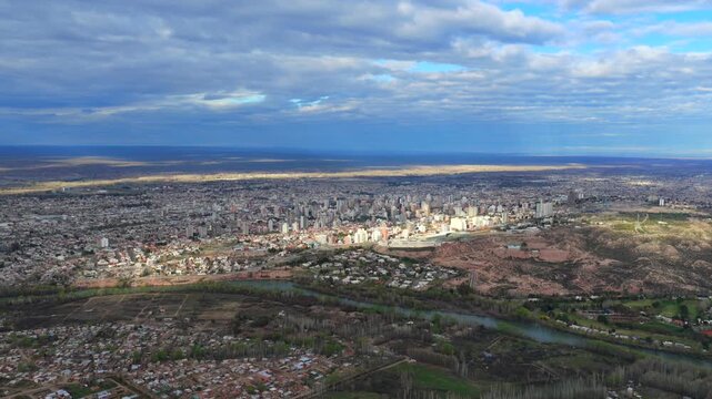 Neuquen city skyline, dense urban districts, Neuquen River, eroded barda terrain, residential neighborhoods and Alto Valle landscape across Patagonia, drone aerial view