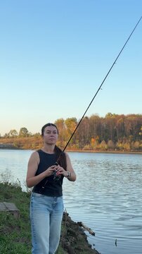 Woman holding a fishing rod on the shore with autumn trees