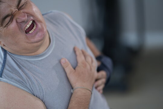 Obese senior man with sudden chest pain lies back on the bench grimacing and holding his heart after physical exertion in the gym. Cardiovascular health and obesity risk concept