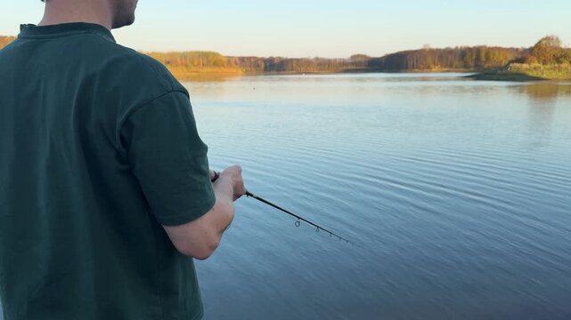 Close view of a man holding a fishing rod beside autumn water