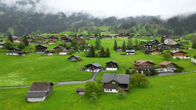 Aerial view of a traditional alpine village with wooden houses on green meadows in foggy hills in Alps