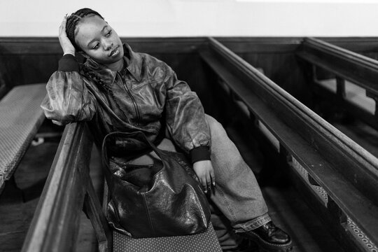 Pensive young woman in leather jacket sitting on a pew