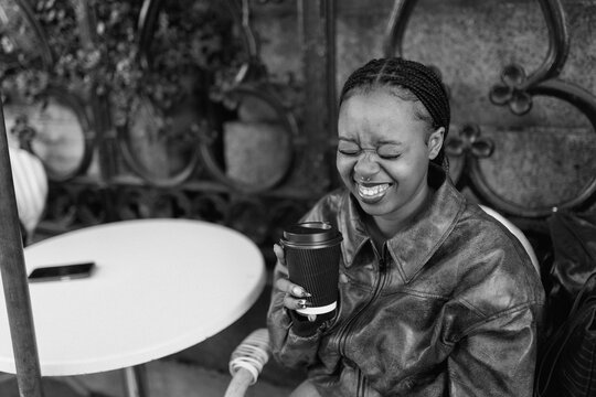 Joyful young black woman laughing with coffee