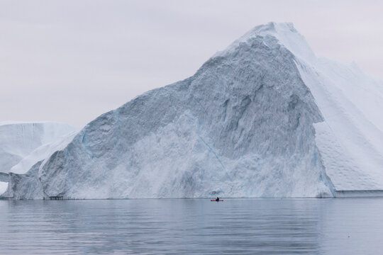 Kayaker dwarfed by giant arctic iceberg on calm water