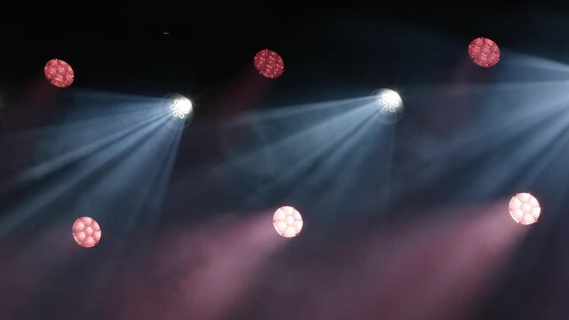 Concert stage lighting with sharp white light beams penetrating through hazy smoke alongside glowing red spots and lens reflections on a dark background
