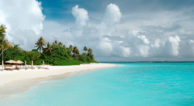 Panoramic view of tropical beach with white sand, palm trees, turquoise ocean water and blue cloudy sky