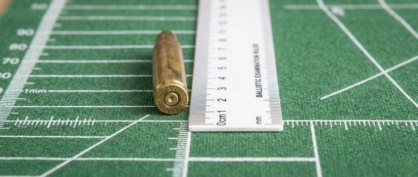 Ammunition bullet measured with a ruler on a green grid background concept of ballistics size and precision