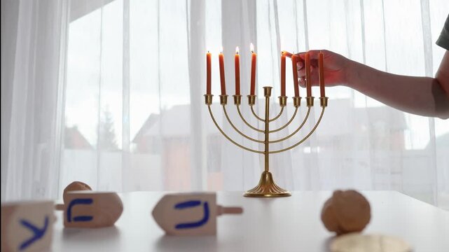 Hand lighting the Hanukkah menorah in a warm daytime home setting