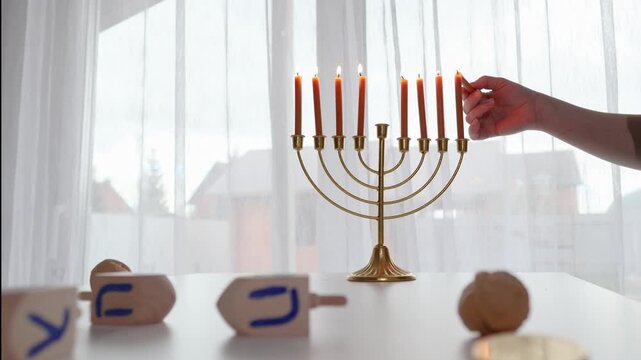 Hanukkah menorah candle lighting in a warm home setting with a hand nearby