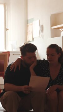 Concerned couple reading important document, wife comforting worried husband feeling stress about bills, mortgage debt, or bad news in a letter at home. Vertical video