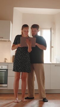 Young couple happily shopping online using a digital tablet together in their modern kitchen, browsing and choosing products for their new home and enjoying togetherness. Vertical video