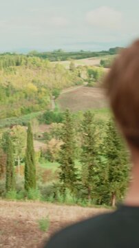 Contemplative bearded man admiring a beautiful tuscan landscape with rolling hills and cypress trees, enjoying nature, serenity, and the peaceful italian countryside. Vertical video 