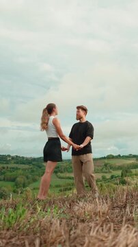 Affectionate young couple sharing a tender moment, holding hands, dancing and kissing in a beautiful rural landscape, enjoying their romantic date and summer vacation together. Vertical video 