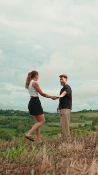 Romantic young couple dancing and kissing in a rural field with a beautiful hilly landscape in the background, enjoying a lovely date in the countryside. Vertical video 