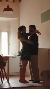 Romantic young couple dancing and kissing at home. Intimate affectionate moment between boyfriend and girlfriend in their kitchen, expressing love and tenderness. Vertical video 