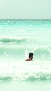 Joyful young man enjoying summer vacation diving and swimming into the turquoise ocean waves, carefree man having fun at the tropical beach during his holiday. Vertical video.