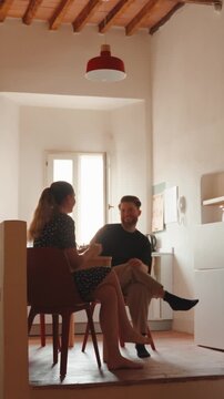 Young couple having an intimate conversation while sitting at a kitchen table in a cozy home, enjoying a relaxed breakfast together and strengthening their bond. Vertical video