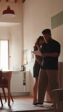 Frustrated man reading a document and arguing with his upset wife about financial problems, the woman getting distressed and leaving the room after their intense discussion. Vertical video