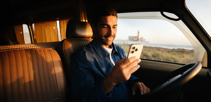 Man smiles while checking his phone inside a van at sunset