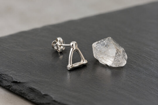 Sterling silver stapes bone earring and quartz crystal on dark slate, jewelry presentation.