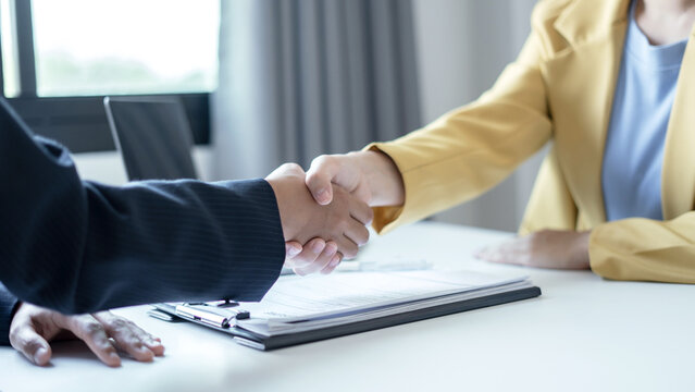Business partners shaking hands over resume document and laptop at desk for job interview success hiring agreement and partnership concept