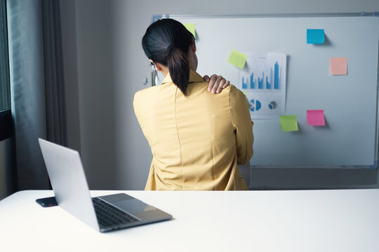 Businesswoman stretching arm and touching shoulder feeling pain while working at desk in office for office syndrome health and wellness concept