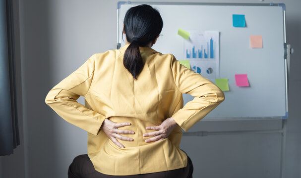 Businesswoman touching her back and shoulder feeling pain from long working hours at office desk for office syndrome health concept