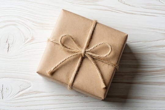 Brown paper gift box tied with jute twine bow on white wooden background. Top view of minimalist present package for birthday holiday. Simple eco friendly packaging for wedding small business craft