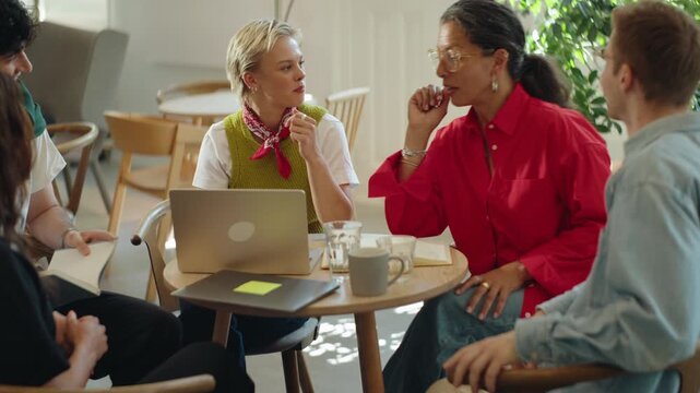 Team gathers for brainstorming and business discussion around a laptop in a coworking cafe, showing collaboration, teamwork, and startup energy in a casual workspace.