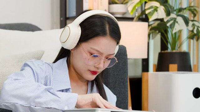 Asian Freelancer Woman Wearing Headphones and Working on Laptop at Home