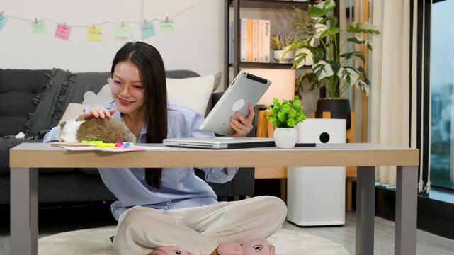 Asian Woman Working on Tablet While Petting Pet Rabbit at Home