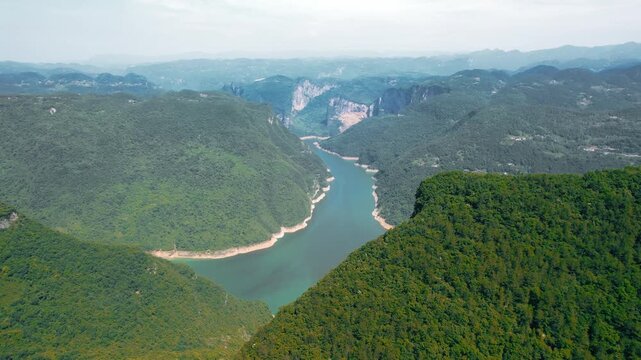 Aerial view of emerald river winding through forested mountains and steep cliffs in Three Gorges, China