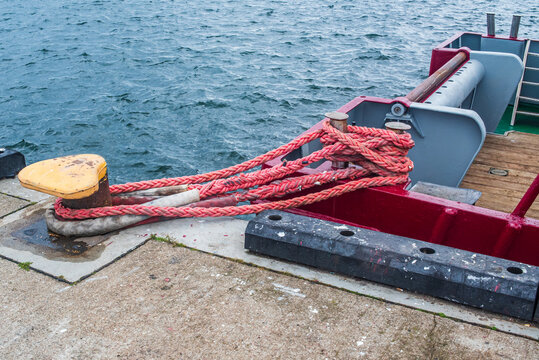 Red mooring rope tied to yellow bollard on pier with vessel docked at sea harbor