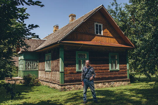 Senior man standing in front of his old wooden childhood home in countryside. Nostalgia, roots, returning home, family heritage, passage of time.  Connection to origins.