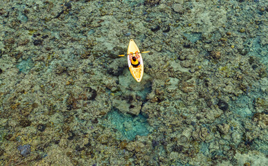 Aerial top view of a woman relaxing on a yellow kayak over a beautiful coral reef in crystal clear turquoise sea water. © SASITHORN