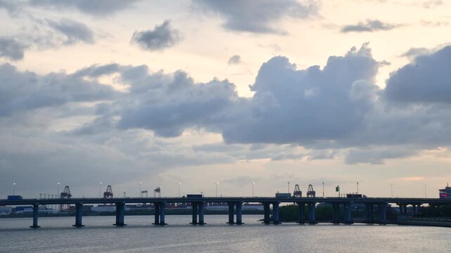 Long Bridge Over Calm Water Under Dramatic Cloudy Sky with Distant Cranes