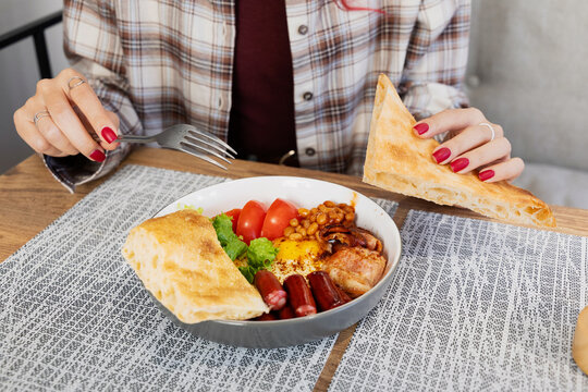 Person enjoying a big breakfast bowl with eggs, sausages, bacon, and a side of flatbread