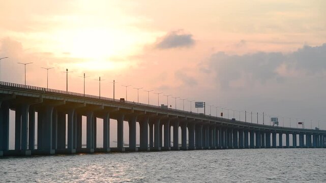 Long Highway Bridge Over Ocean at Sunset with Silhouetted Streetlights and Cloudy Sky