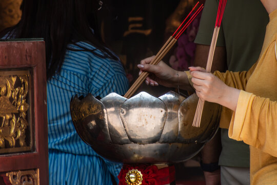 Hands holding traditional joss sticks during prayer and spiritual ritual in an Asian temple